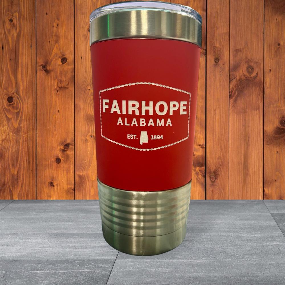 The 20oz. Stainless Tumbler with Silicone Grip, featuring a red and stainless steel design and double-wall vacuum insulation, displays the text "Fairhope Alabama, Est. 1894" against a wooden backdrop.