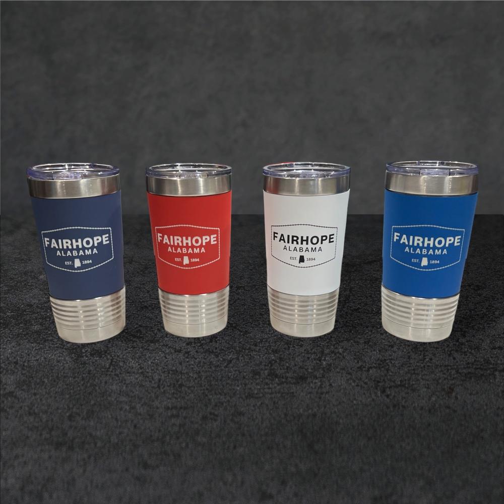 Four 20oz. stainless tumblers with double-wall vacuum insulation and colored silicone grip sleeves, featuring the text "Fairhope Alabama." The sleeve colors from left to right are navy blue, red, white, and blue.