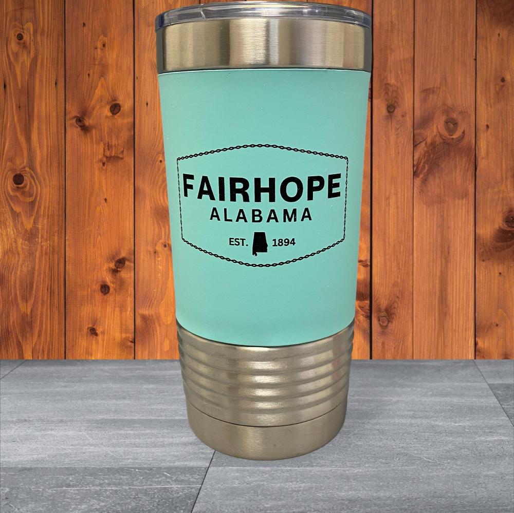 This 20oz. Stainless Tumbler with Silicone Grip features a light blue design, silver lid and base, and the text "Fairhope Alabama Est. 1894" against a wooden background. The double-wall vacuum insulation ensures superior temperature control for your beverages.