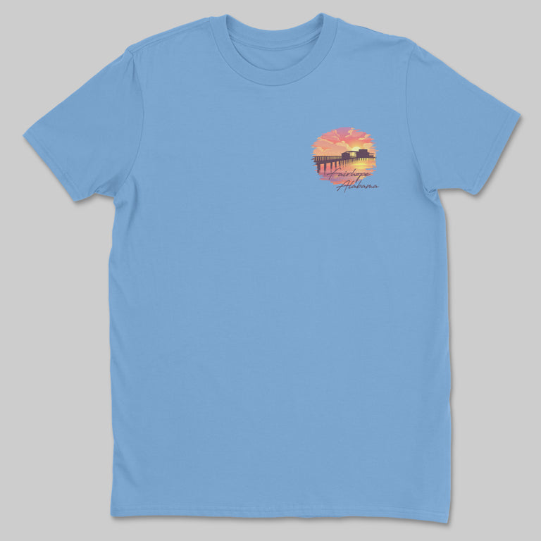 Light blue "Fairhope Sunset - Tee" featuring a sunset graphic with a silhouette of Fairhope Pier and the text "Alabama.